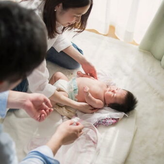 Image of a mother and father kneeling down playing with a baby on the carpet